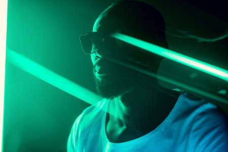 Rap star. Cinematic portrait of stylish young man in neon lighted room. Bright neoned colors. African-american model, musician indoors. Youth culture in party, festival style and music concept.の写真素材