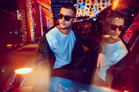 Reflection. Cinematic portrait of stylish young man in neon lighted room. Bright neoned colors....