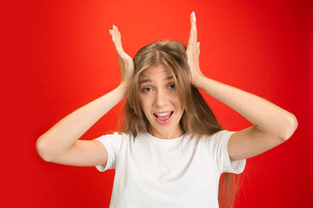 Shocked. Portrait of young caucasian woman with bright emotions on red studio background with copyspace. Blonde model. Concept of human emotions, facial expression, sales, advertising, youth.の写真素材