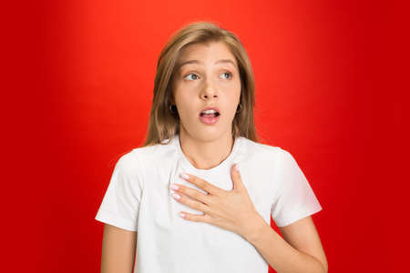 Stressed, shocked. Portrait of young caucasian woman on red studio background with copyspace. Blonde female model. Concept of human emotions, facial expression, sales, advertising, youth.の写真素材