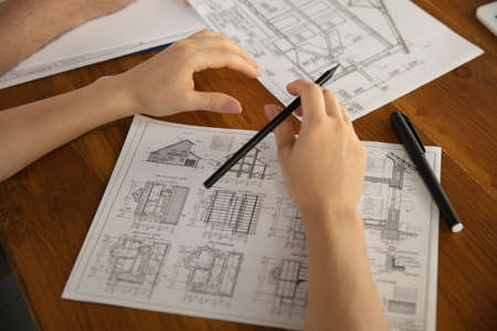 Close up hands of architect-engineer and young couple during presentation of future house. Top view...