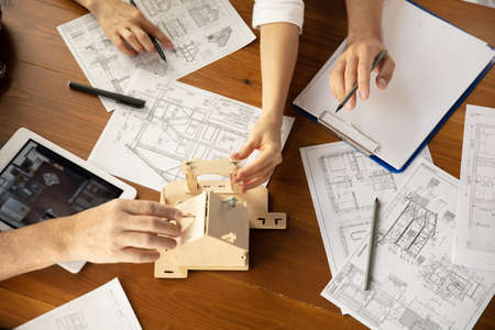 Top view hands of architect-engineer and young couple during presentation of future house. Top view table with documents, blueprint. First home, industrial, building concept. Moving to new live place.の写真素材