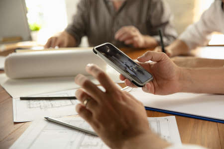 Close up hands of architect-engineer and young couple during presentation of future house. Top view table with documents, blueprint. First home, industrial, building concept. Moving to new live place.の写真素材