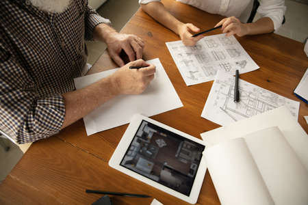 Close up hands of architect-engineer and young couple during presentation of future house. Top view...