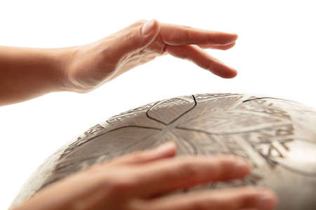 A close up of hands playing the hank drum on white studio background. Concept of hobby, professional occupation, music, traditions, festival. Copyspace for your ad. Ethnic instrument.の写真素材