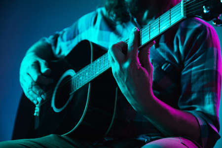 Close up of guitarist hand playing guitar, macro. Concept of advertising, hobby, music, festival, entertainment. Person improvising inspired. Copyspace to insert image or text. Colorful neon lighted.の写真素材