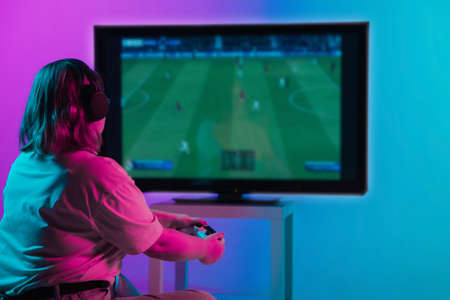Back view shot of professional gamer playing online video game on her personal computer. Room lit in...