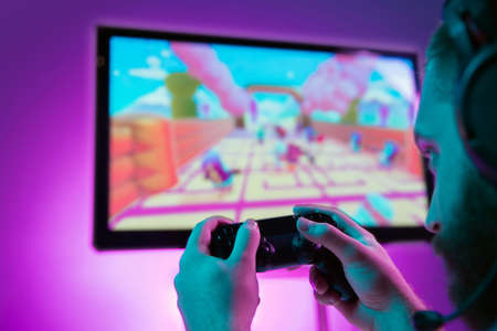 Back view close up of professional gamer playing online video game with his gameset. Room lit in neon light and retro style. Using headphones to talk with the team. Entertainment, fun concept.の写真素材