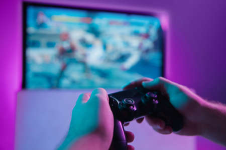 Back view close up of professional gamer playing online video game with his gameset. Room lit in...