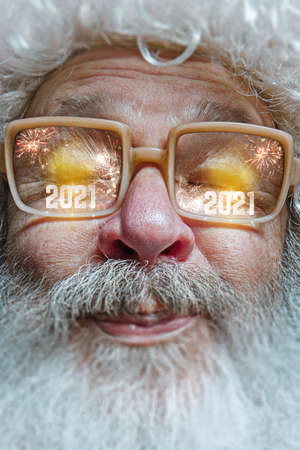 Close up shot of Santa Claus in stylish glasses with a reflection of 2021 Happy New Year and salute. Looks delighted, shocked, astonished, emotional. Facial expression, emotions, Christmas, winter mood.の写真素材