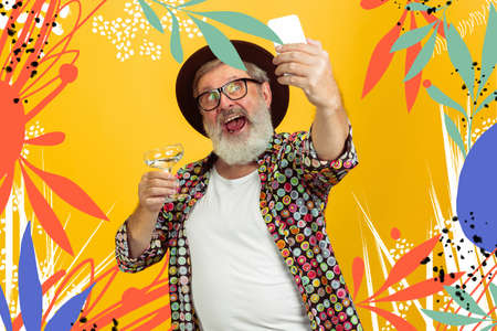 Forever young. Portrait of senior hipster man using devices, gadgets isolated on orange studio...