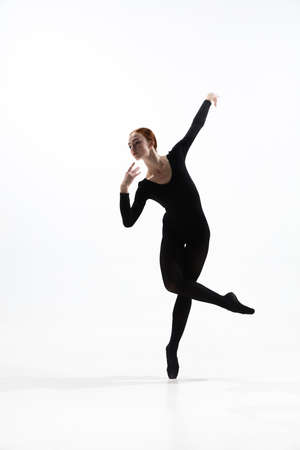 Light. Young and graceful ballet dancer in minimal black style isolated on white studio background. Art, motion, action, flexibility, inspiration concept. Flexible caucasian ballet dancer.の写真素材