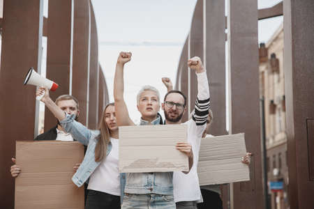 Upcoming. Group of activists giving slogans in a rally. Caucasian men and women marching together in a protest in the city. Look angry, hopeful, confident. Blank banners for your design or ad.の写真素材