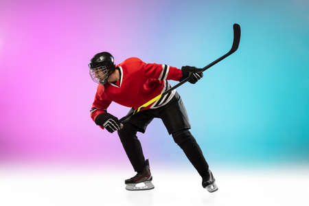 On fire. Male hockey player with the stick on ice court and neon gradient background. Sportsman wearing equipment, helmet practicing. Concept of sport, healthy lifestyle, motion, wellness, action.の写真素材