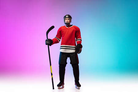 First. Male hockey player with the stick on ice court and neon gradient background. Sportsman...