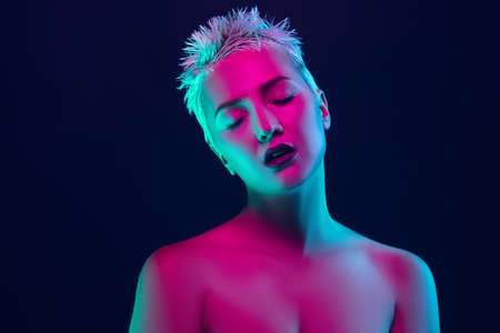 Shiny. Portrait of female fashion model in neon light on dark studio background. Beautiful caucasian...