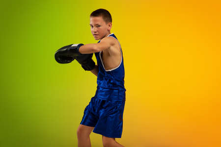 Force. Teenage professional boxer training in action, motion isolated on gradient background in neon light. Kicking, boxing. Concept of sport, movement, energy and dynamic, healthy lifestyle.の写真素材