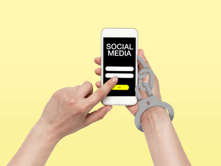 Hand using smartphone, device on top view. Addicted man, wired with chain to social media on the screen with login frame. Technologies, modern, marketing, online. Yellow color on background.の写真素材