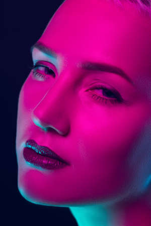 Close up. Portrait of female fashion model in neon light on dark studio background. Beautiful caucasian woman with trendy make-up and well-kept skin. Vivid style, beauty concept. Close up. Copyspaceの写真素材