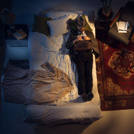 Right. Portrait of a businessman, accountant sleeping in the bed at home. Top view. Dressed office worker, financist sleeping after tiring wotk day. Holding his case close to. Workaholic. Job.の写真素材