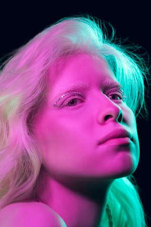 Princess. Close up portrait of beautiful albino girl on dark background in neon light. Blonde female...