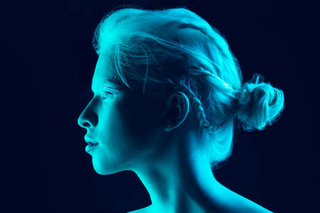 Night. Close up portrait of beautiful albino girl on dark background in neon light. Blonde female...