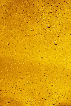 Close up view of cold drops on the glass of beer background. Texture of cooling alcohol drink with macro bubbles on the glass wall. Fizzing or floating up to top of surface. Golden colored.の写真素材