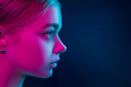 Profile. Portrait of female fashion model in neon light on dark studio background. Beautiful caucasian woman with trendy make-up and well-kept skin. Vivid style, beauty concept. Close up. Copyspaceの写真素材