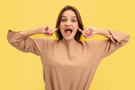 Closing ears. Portrait of young caucasian woman isolated on yellow studio background with copyspace....