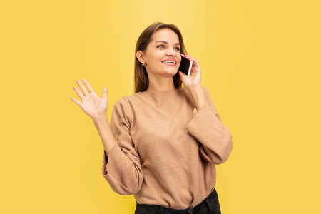 Talking phone. Portrait of young caucasian woman isolated on yellow studio background with copyspace. Beautiful female model. Concept of human emotions, facial expression, sales, advertising, youth.の写真素材