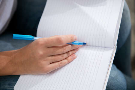 Close up female hands writing. Remote working from home. Workplace in home office on sofa with laptop and devices. Concept of distance learning, isolation, female business, shopping online, conference.の写真素材