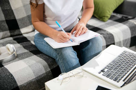 Close up female hands writing. Remote working from home. Workplace in home office on sofa with...