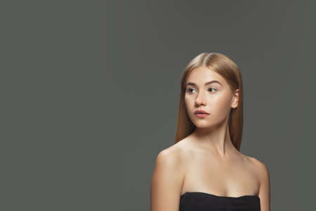 Youth. Beautiful model with long smooth, flying blonde hair on dark grey studio background. Young caucasian model with well-kept skin and hair blowing on air. Concept of salon care, beauty, fashion.の写真素材