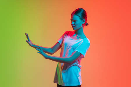 Scared stopping, rejecting. Young caucasian girls portrait on gradient green-orange studio background in neon light. Concept of youth, human emotions, facial expression, sales, ad.の写真素材