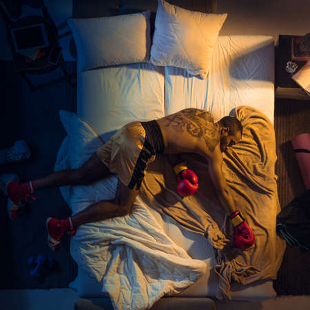 Kicking. Top view of young professional boxer, fighter sleeping at his bedroom in sportwear with gloves. Loving his sport even more than comfort, playing match even if resting. Action, motion, humor.の写真素材