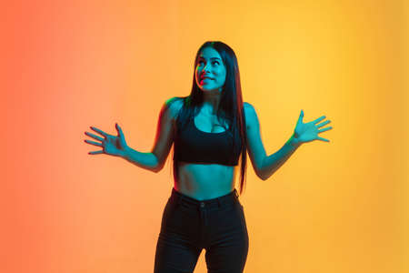 Shocked. Young caucasian womans portrait on gradient yellow-orange studio background in neon light....