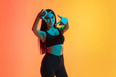 Framing. Young caucasian womans portrait on gradient yellow-orange studio background in neon light....