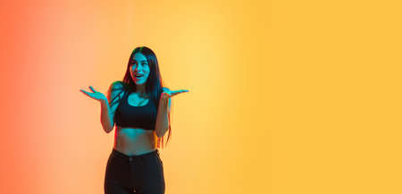 Astonished. Young caucasian womans portrait on gradient yellow-orange studio background in neon...