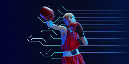 Teenager in sportswear boxing isolated on blue studio background in neon light. Novice male caucasian boxer training hard and working out, kicking. Neoned modern artwork, cover, flyer designed.の写真素材