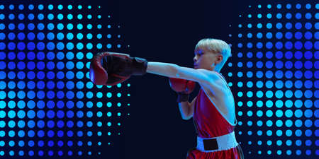 Teenager in sportswear boxing isolated on navy dotted studio background in neon light. Working out,...