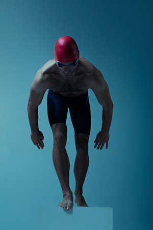 Professional caucasian male swimmer with hat and goggles practicing and training isolated on blue neoned studio background. Grace of motion and action. Healthy lifestyle, sport and movement concept.の写真素材