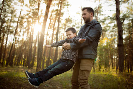 Emotions. Father and son walking and having fun in autumn forest, look happy and sincere. Laughting, playing, having good time together. Concept of family, happiness, holidays, childhood, lifestyle.の写真素材