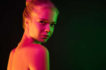 Secretly. Portrait of female fashion model in neon light on dark studio background. Beautiful caucasian woman with trendy make-up and well-kept skin. Vivid style, beauty concept. Close up. Copyspaceの写真素材