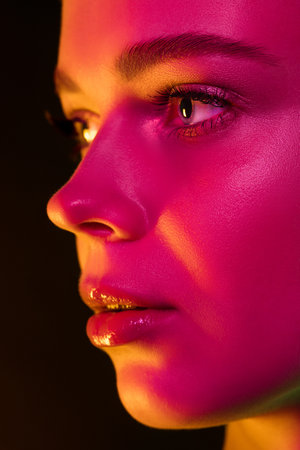 Skin glow. Portrait of female fashion model in neon light on dark studio background. Beautiful caucasian woman with trendy make-up and well-kept skin. Vivid style, beauty concept. Close up.の写真素材