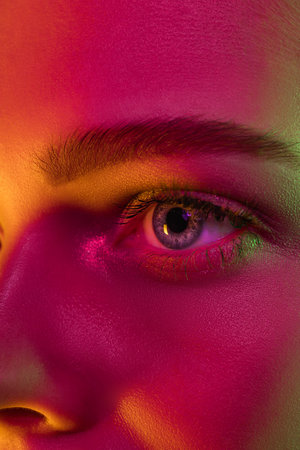Eyes. Portrait of female fashion model in neon light on dark studio background. Beautiful caucasian woman with trendy make-up and well-kept skin. Vivid style, beauty concept. Close up.の写真素材