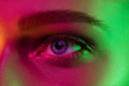 Eyes. Portrait of female fashion model in neon light on dark studio background. Beautiful caucasian woman with trendy make-up and well-kept skin. Vivid style, beauty concept. Close up.の写真素材