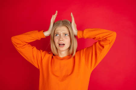 Angry holding head in hands. Portrait of young caucasian woman isolated on red studio background...
