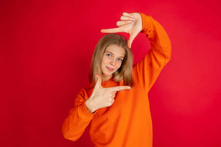 Framing face with hands. Portrait of young caucasian woman isolated on red studio background with...