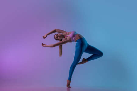 Graceful. Young sportive woman training isolated on gradient studio background in neon light. athletic and graceful. Modern sport, action, motion, youth concept. Beautiful caucasian woman practicing.の写真素材