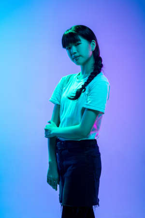 Posing. Young asian womans portrait on gradient blue-purple studio background in neon light. Concept...